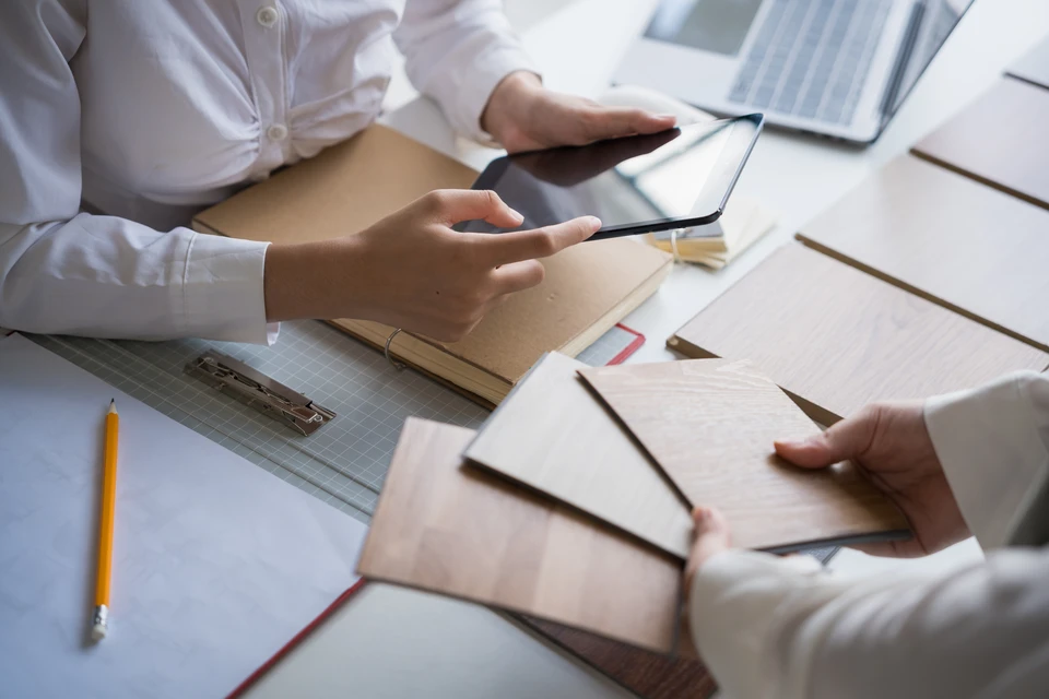 Photographie d'une équipe de professionnels (conception/installateurs) en tenue de travail professionnelle discutant avec un couple de clients dans un espace d'aménagement intérieur (cuisine ou salle de bain en cours de rénovation). Les professionnels sont engagés dans une discussion constructive, consultant des plans ou documents, montrant l'écoute et le suivi personnalisé mentionnés dans le texte. L'atmosphère doit être collaborative, professionnelle et bienveillante.