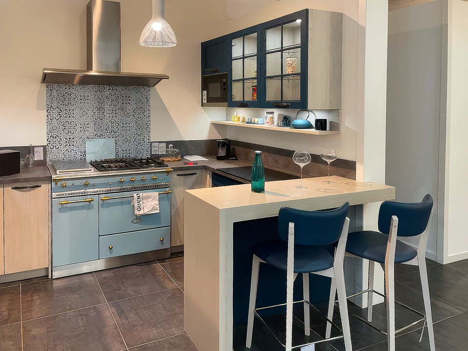 Fa&ccedil;ade moderne d'un showroom d'am&eacute;nagement int&eacute;rieur situ&eacute; dans une zone commerciale, avec une large devanture vitr&eacute;e illumin&eacute;e pr&eacute;sentant des am&eacute;nagements de cuisine et salle de bain en vitrine, parking accessible devant le b&acirc;timent, carrefour routier visible indiquant une bonne accessibilit&eacute; routi&egrave;re, clients se dirigeant vers l'entr&eacute;e du magasin en journ&eacute;e. Photo prise de face, mettant en avant la fa&ccedil;ade accueillante et la localisation dans une zone facilement accessible.