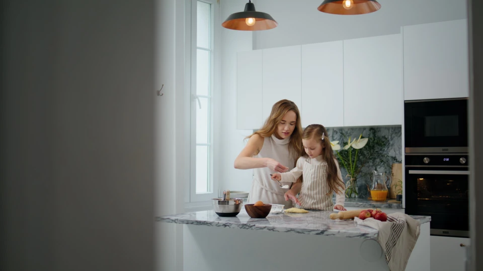 Jeune femme en tablier noir travaillant sur ordinateur portable dans cuisine professionnelle moderne, t&eacute;l&eacute;phone &agrave; l'oreille, prenant des notes