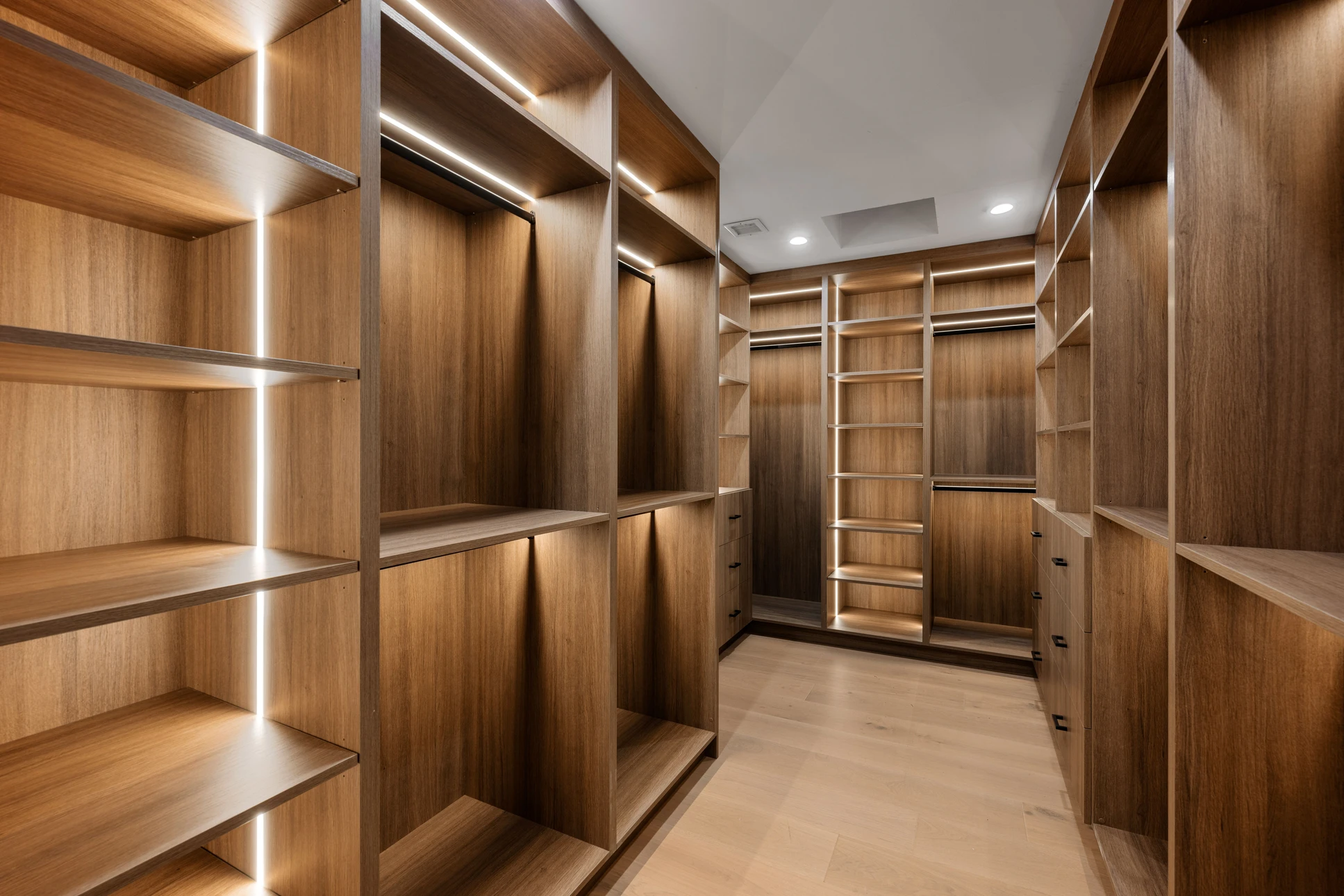 Dressing spacieux en bois clair avec étagères ouvertes, tringles à vêtements avec éclairage LED intégré et tiroirs coulissants partiellement ouverts