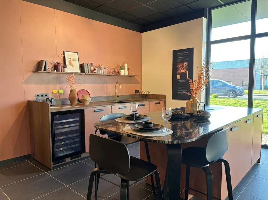 Cuisine moderne ouverte, coloris bordeaux mat, îlot central arrondi avec plan de travail blanc et étagères en bois naturel